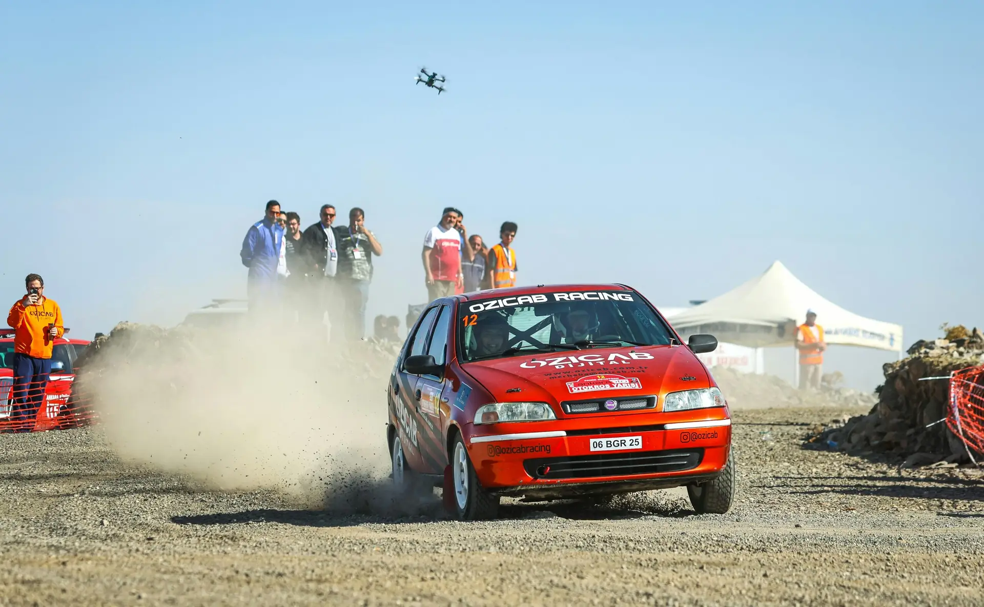 Fiat Palio rally car racing on a dusty track with spectators nearby.